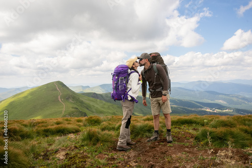 Happy couple tourists with backpacks in mountains enjoying panoramic on view of sunny mountains during a hike in the national . Travel  happiness emotion  summer holiday concept