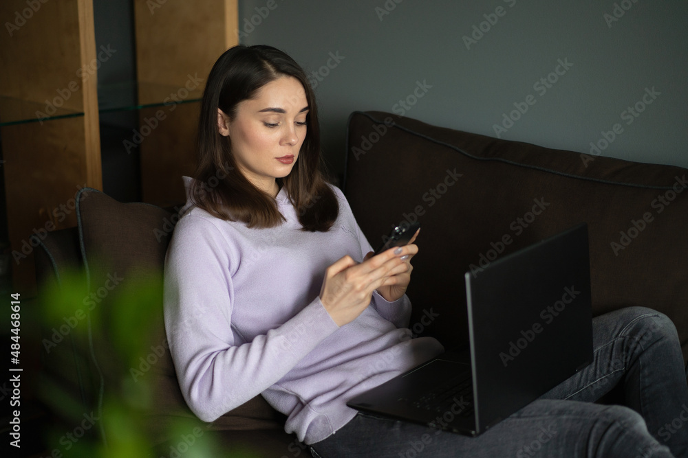 A girl are talking on the phone and working laptop and sits on the sofa A girl are talking on the phone and working laptop and sits on the sofa