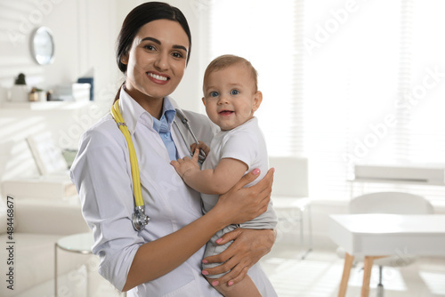 Young pediatrician with cute little baby in clinic. Space for text