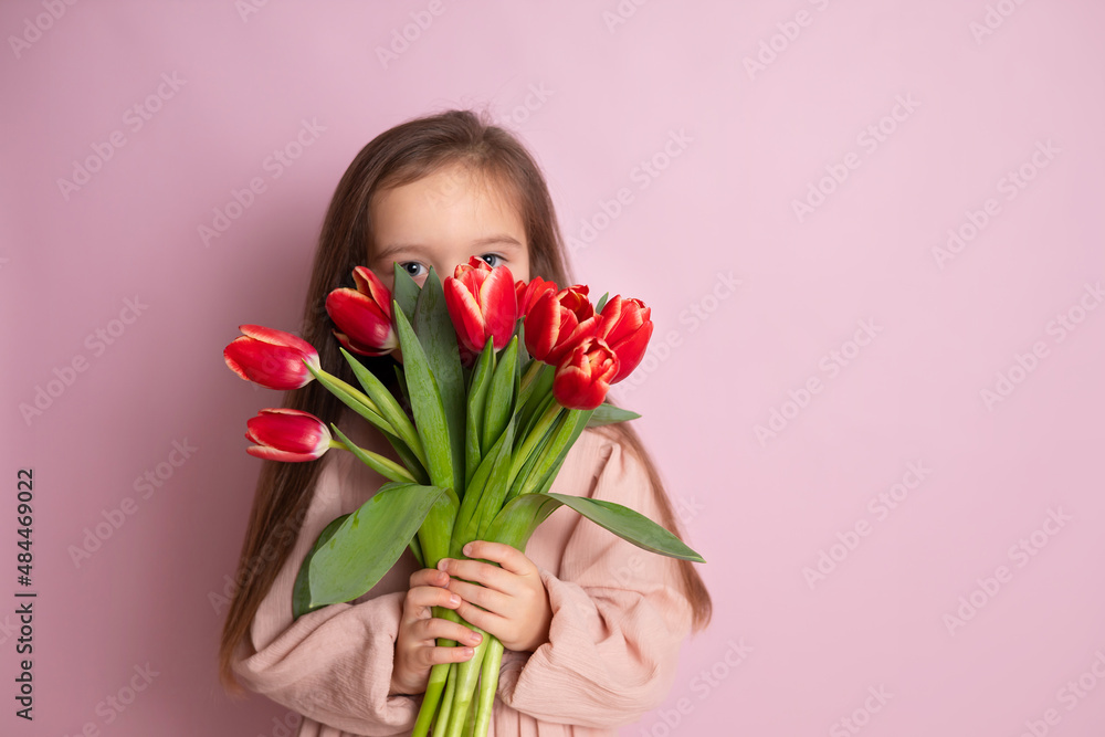A little cute girl holding a bouquet of tulips and sniffing them Pink background. Happy women's day. Space for text. Bright Emotions.