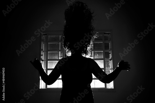 Silhueta sinistra de uma pessoa em contraluz na frente de uma janela em um quarto escuro. photo