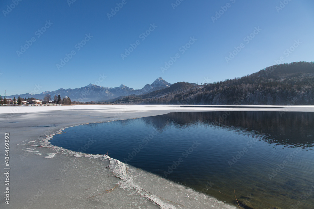 dyllic sunny winter landscape at the north bank of the nearly frozen lake Weissensee  with a beautiful panorama view to the Füssen mountains and the twin peak mountain Säuling in the region Allgäu