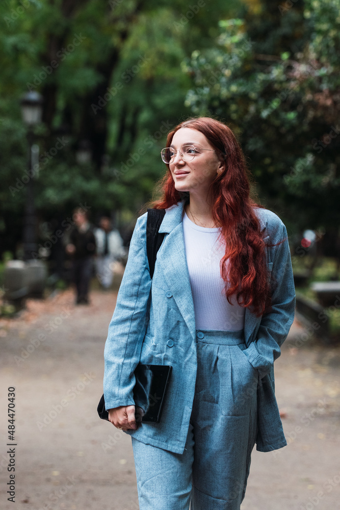 Attractive young businesswoman wearing blue suit holding digital tablet outdoors, professional female architect walking at park Attractive young businesswoman wearing blue suit holding digital tablet outdoors, professional female architect walking at park