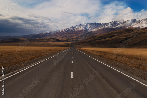An empty asphalt road stretching into the distance through the Altai Mountains.