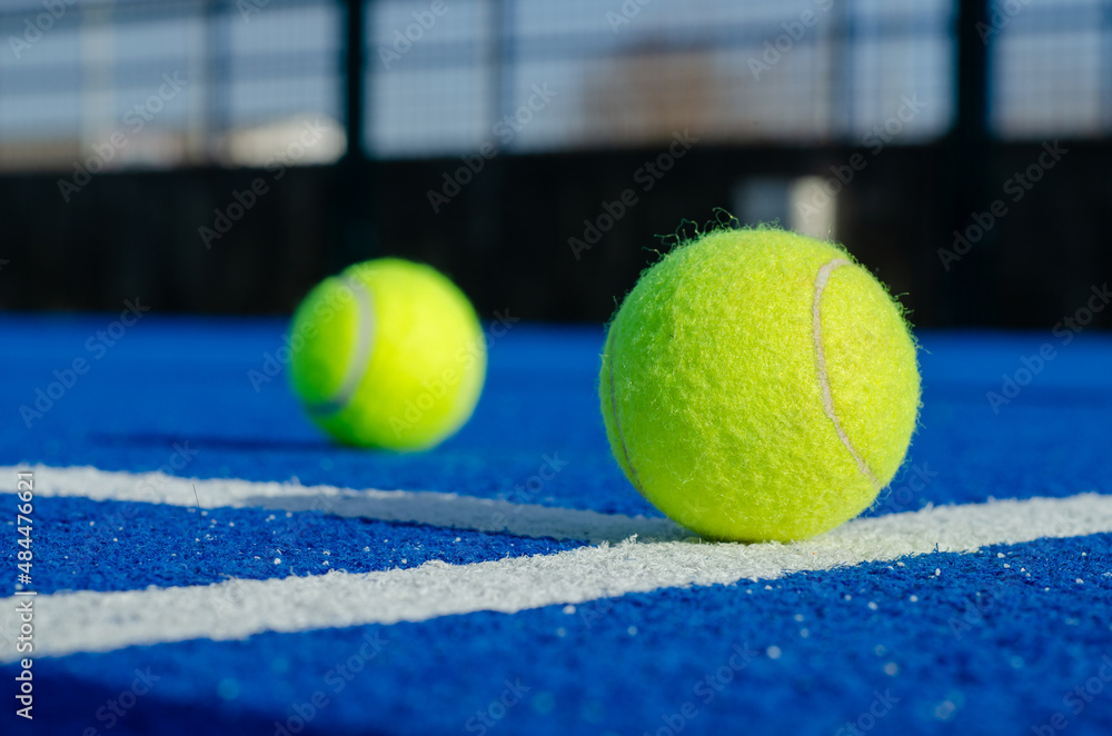 Ground level image of two balls on a blue paddle tennis court lines