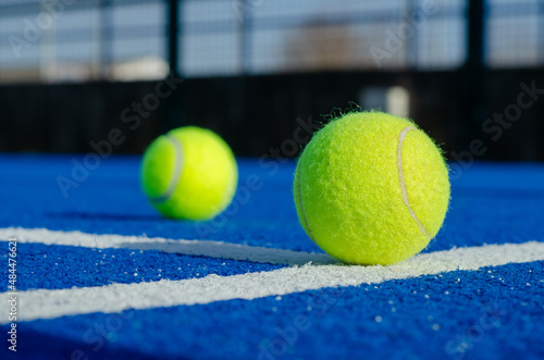 Ground level image of two balls on a blue paddle tennis court lines © Vic