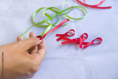 Cintas de colores, cintas para campañas de lucha contra el cáncer y el SIDA. Manos preparando cintas rojas y verdes. Campaña roja de concientización sobre el VIH