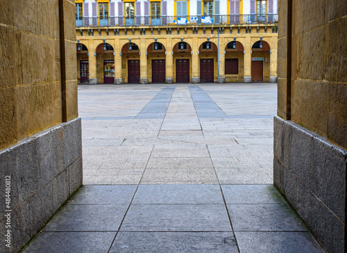 View of the Plaza de la Constitución from the alley on one side, under an arch of the square in the middle of the side, in the background, the arches in front, the balconies with the Donostiarra flag  photo