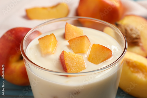 Tasty peach yogurt with pieces of fruit in glass on table, closeup