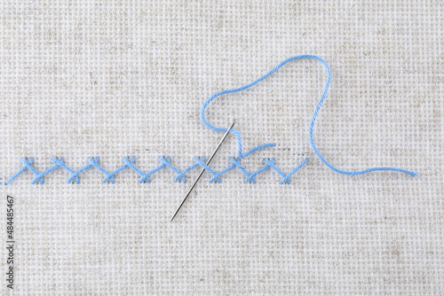 Embroidery stitches made with light blue thread and needle on canvas, top view photo