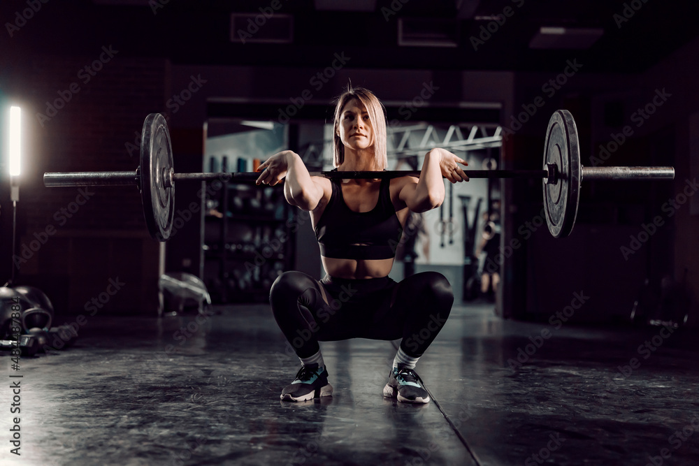 A female bodybuilder crouching at the gym and lifting barbell. A female bodybuilder crouching at the gym and lifting barbell.