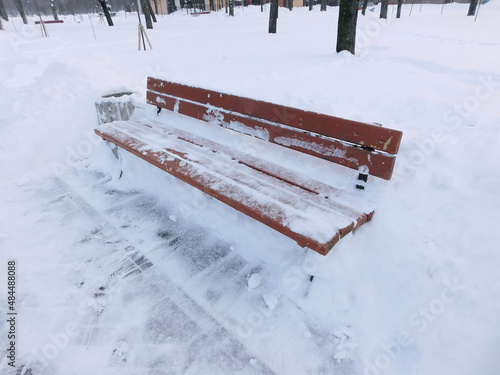 A bench in the park brought by a large layer of snow.