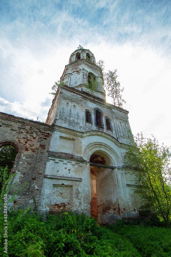 Side view of the courtyard facade of the bell tower of an old, destroyed and abandoned church in Russia. Walls with peeling paint and old red bricks. Trees on the roofs. Summer. Daylight. Side view of the courtyard facade of the bell tower of an old, destroyed and abandoned church in Russia. Walls with peeling paint and old red bricks. Trees on the roofs. Summer. Daylight.