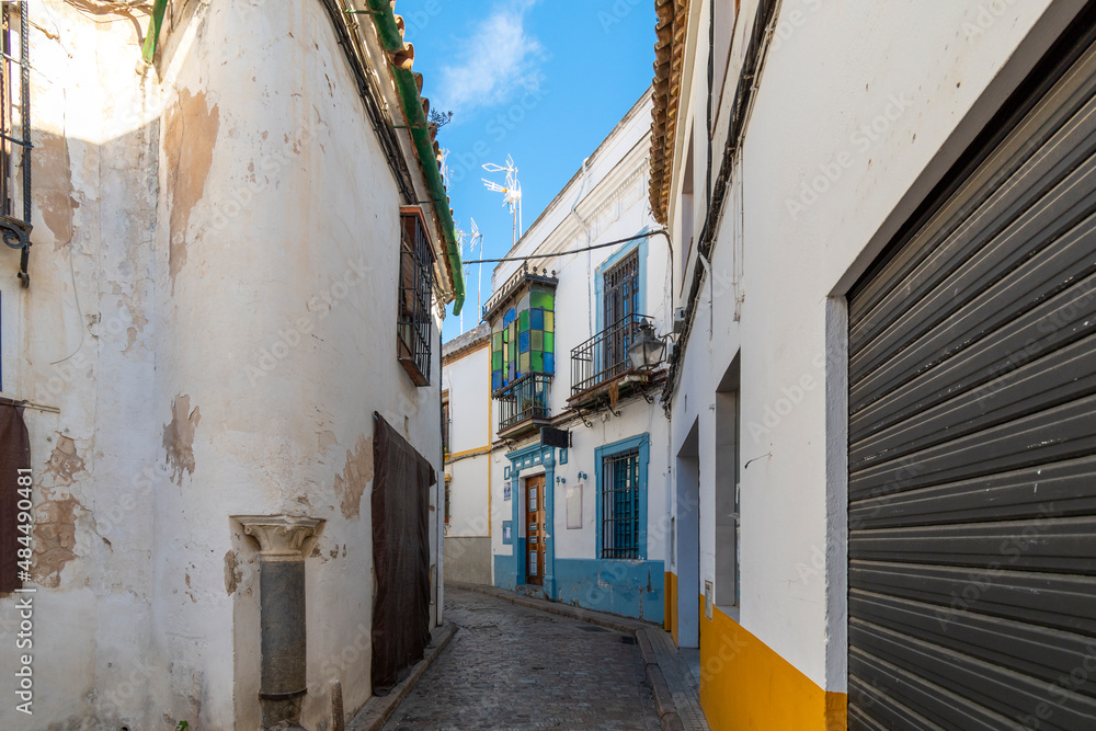 A narrow alley or road through the Jewish quarter with white walls and colorful accents in the historic old town village center of Cordoba, Spain.