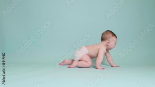 Happy toddler baby crawling on studio blue background. Funny child boy at the age of six months with a smile on his face, copy space photo