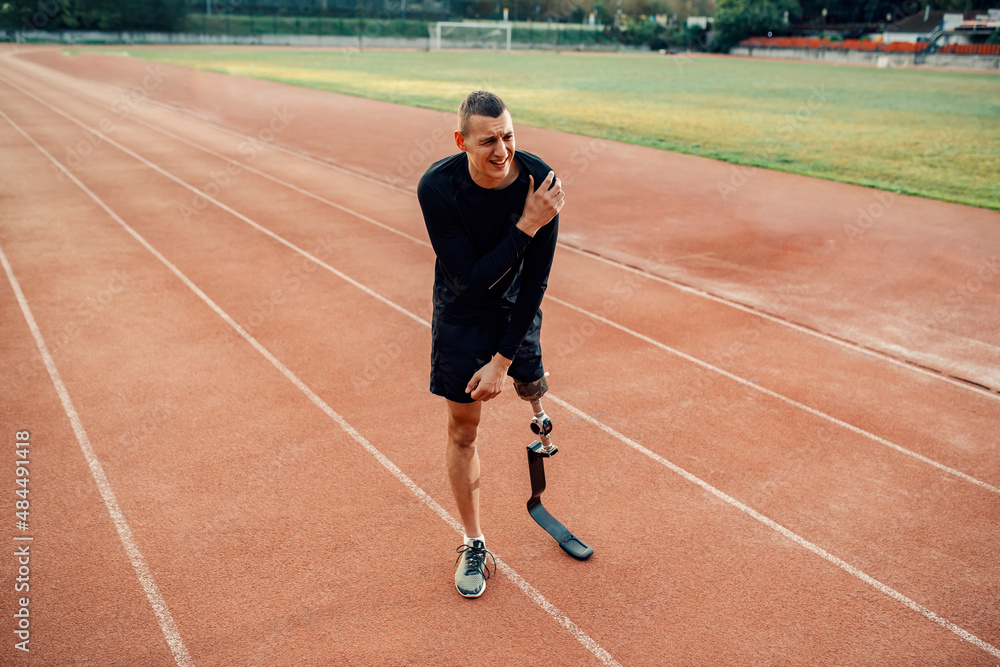 A sportsman with artificial leg have painful shoulder injury while standing at stadium, A sportsman with artificial leg have painful shoulder injury while standing at stadium,