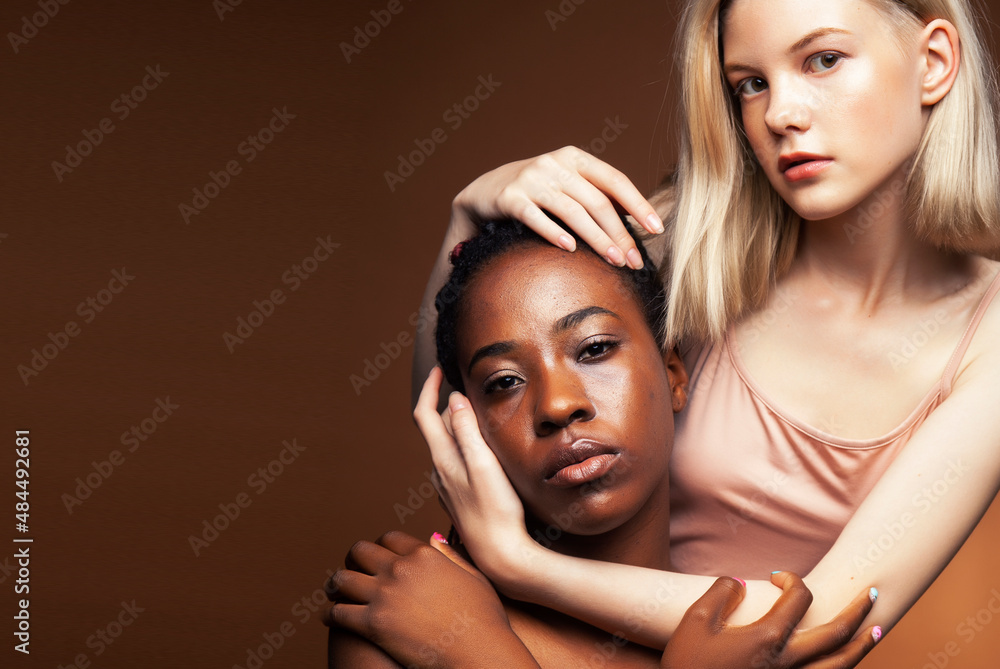 Fototapeta premium two pretty girls african and caucasian blond posing cheerful together on brown background, ethnicity diverse lifestyle people concept