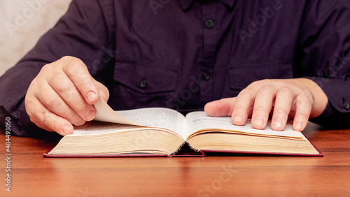A man reads the Bible while sitting at a table. An open book in the hands of a man