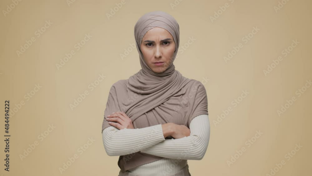Portrait of young offended middle eastern lady wearing traditional hijab posing with folded arms and looking grumpily Portrait of young offended middle eastern lady wearing traditional hijab posing with folded arms and looking grumpily