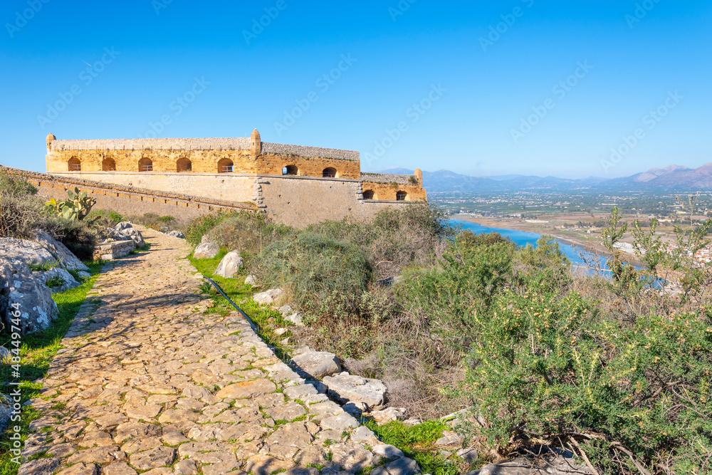 Walls and structures at the hilltop Fortress of Palamidi above the town of Nafplio in the Peloponnese region of Southern Greece on a clear summer day with the sea and beach in view below.