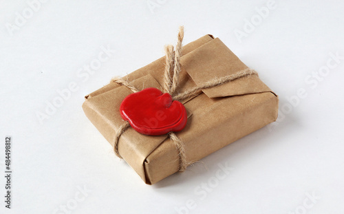 mail parcel wrapped in craft paper and sealed with a red wax seal on a white background. Packet with wax seal, gift box with wax seal