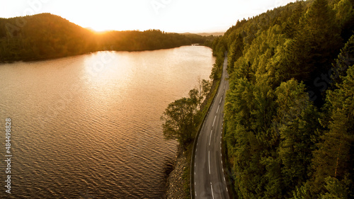 Sun coming over the tree line at the break of dawn with a winding road finding its way into the horizon. 