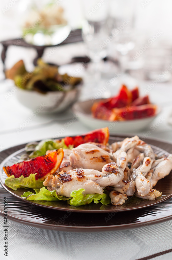 Grilled Frog Legs Garnished with Blood Orange Slices and Fresh Lettuce