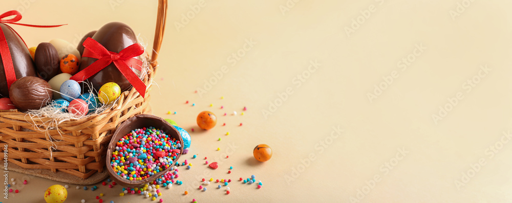 Basket with chocolate Easter eggs, candies and sprinkles on beige background with space for text