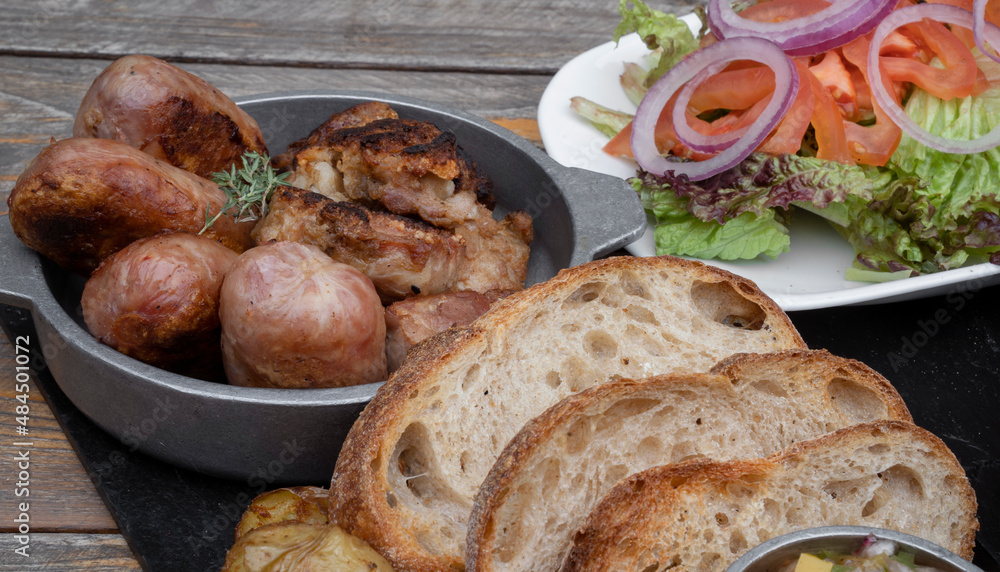 Traditional asado criollo plate. Closeup view of chorizos, pork sausages, grilled sweetbreads, potatoes, bread, and a traditional salad with lettuce, tomato and onion. Traditional asado criollo plate. Closeup view of chorizos, pork sausages, grilled sweetbreads, potatoes, bread, and a traditional salad with lettuce, tomato and onion.