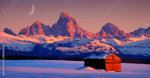Tetons Mountains at Sunset in Winter with Old Cabin Homestead Building and Rising Cresent Moon