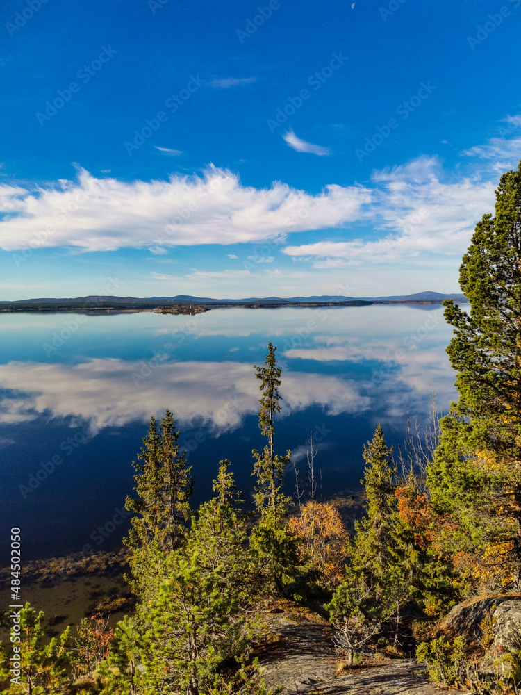 Obraz premium The White Sea coast with trees in the foreground and stones in the water on a sunny day. Karelia.