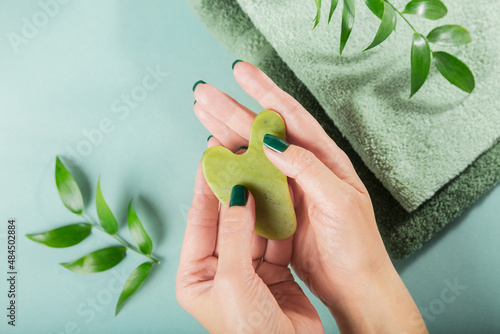 Fototapeta Naklejka Na Ścianę i Meble -  Female hand holding massage gua sha scraper for the face of green jade stone