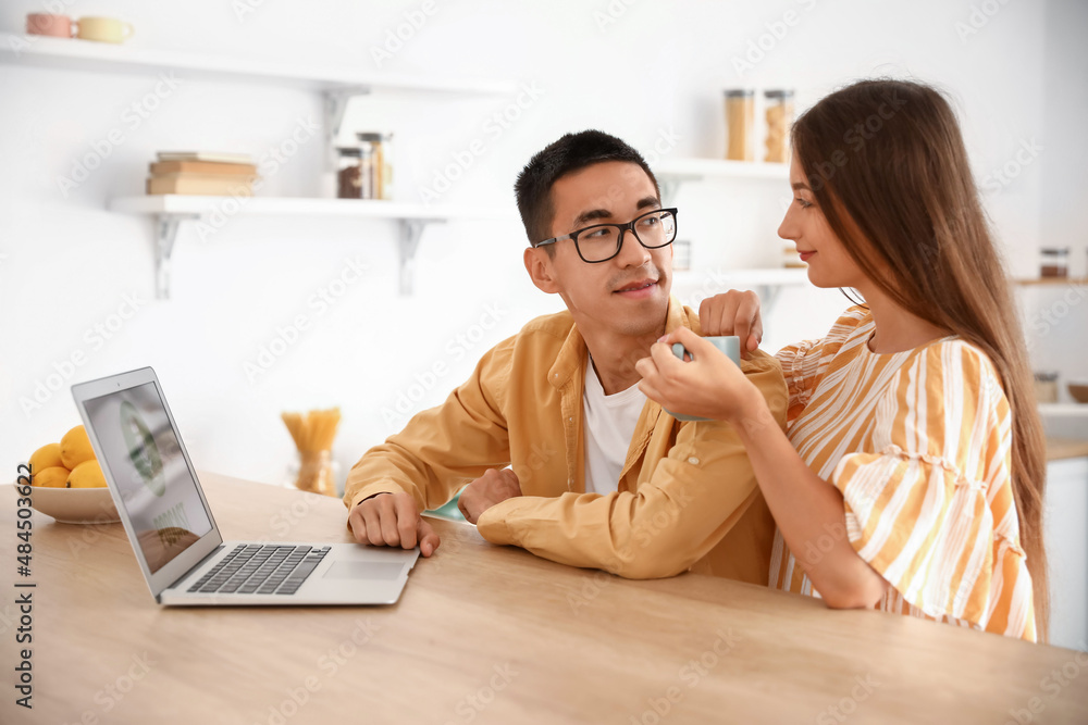 Young couple using laptop at table in kitchen Young couple using laptop at table in kitchen