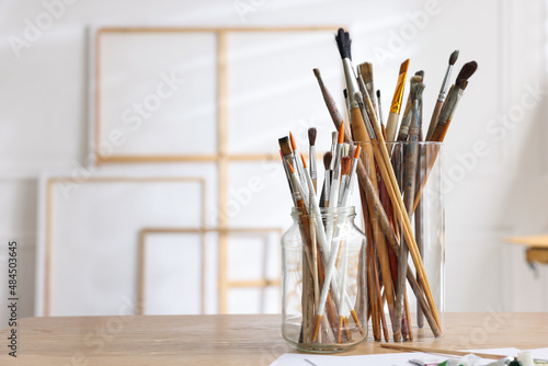 Holders with different paintbrushes on wooden table in studio, space for text. Artist's workplace