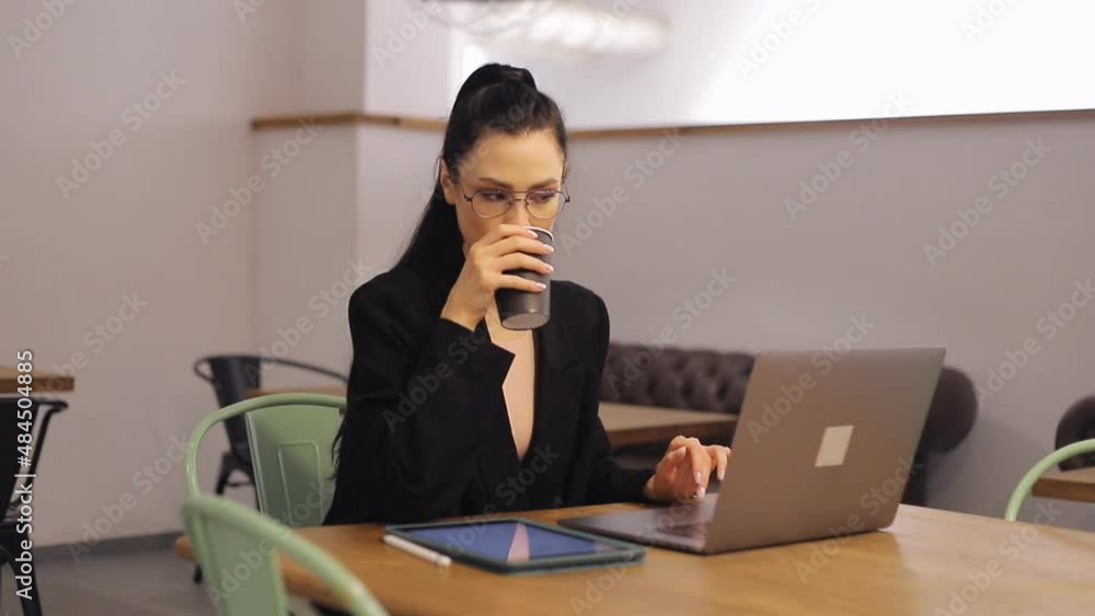 Young freelancer woman working on laptop and drinking coffee from paper cup Young freelancer woman working on laptop and drinking coffee from paper cup