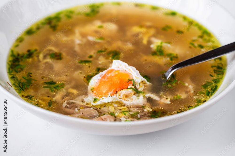 Poultry soup with meat, garlic and poached egg in white plate.