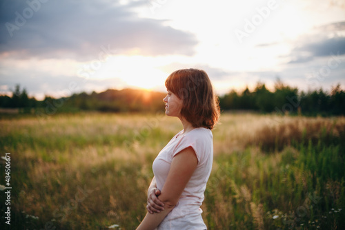 Beautiful girl standing in a field at sunset 