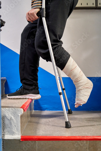 Unrecognizable man with crutches and broken leg climbs the stairs at home