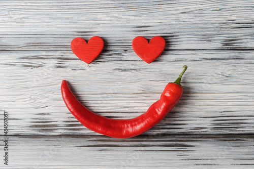 Red Valentine’s hearts and hot pepper located as smilng face on aged white wooden background
