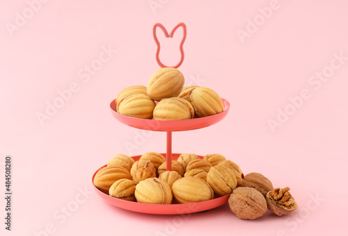 Dessert stand of tasty walnut shaped cookies with boiled condensed milk on pink background