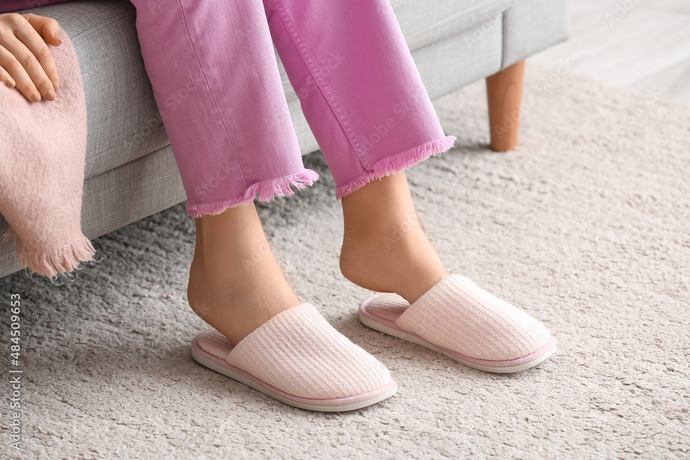 Young woman in soft comfortable slippers sitting on sofa at home Young woman in soft comfortable slippers sitting on sofa at home