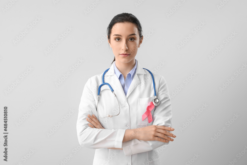 Female oncologist with pink ribbon on light background. Breast cancer awareness concept Female oncologist with pink ribbon on light background. Breast cancer awareness concept