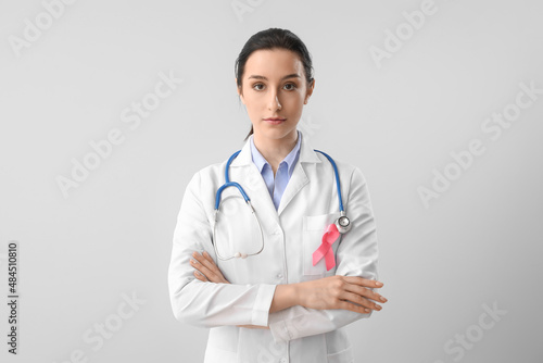 Female oncologist with pink ribbon on light background. Breast cancer awareness concept