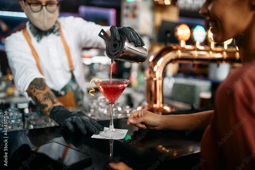 Close-up of barman serves cocktail to female guest at bar counter.