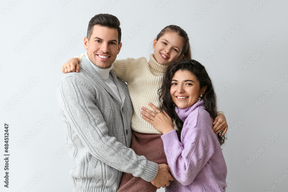 Happy little girl and her parents in warm sweaters on light background