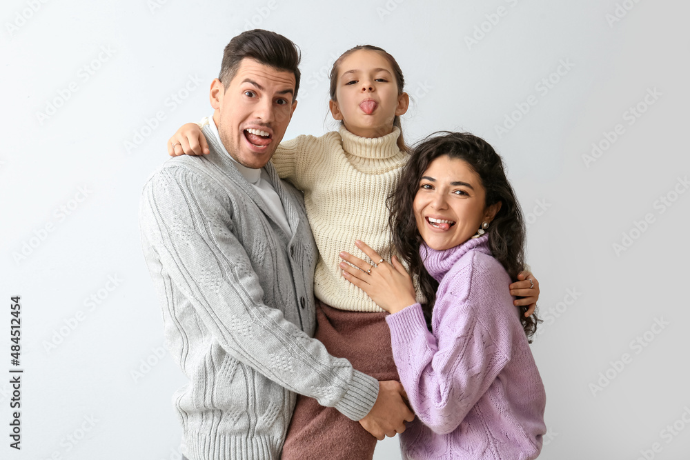 Little girl and her parents in warm sweaters showing tongues on light background Little girl and her parents in warm sweaters showing tongues on light background