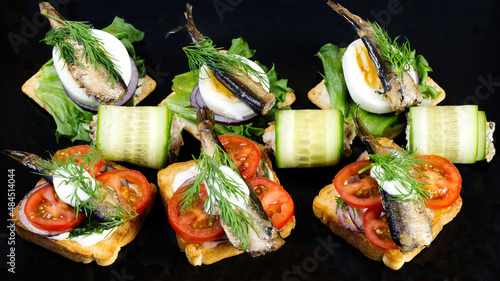 a delicious snack on a black plate. Toast with sprats, egg, tomatoes and onions. close up