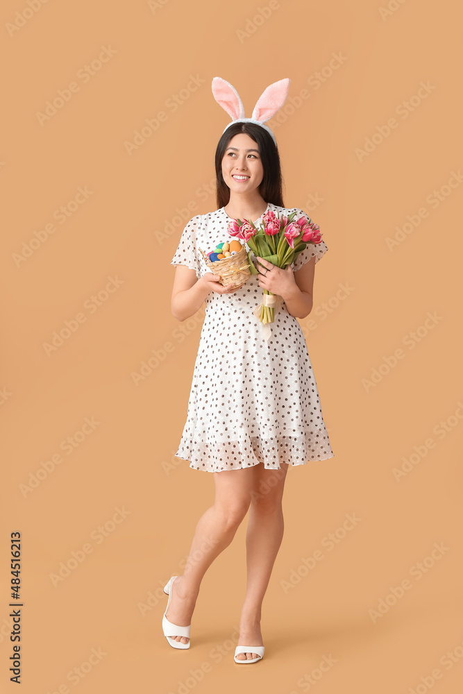 Beautiful Asian woman with bunny ears and Easter basket on color background