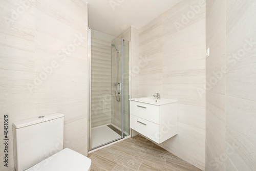 Simple bathroom with white wooden furniture  glass-enclosed shower stall and white toilet bowls