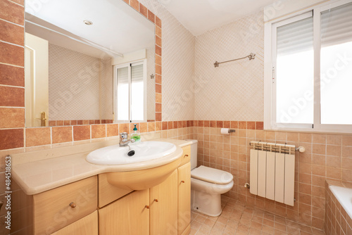 Bathroom with light colored wooden cabinets and reddish and cream colored tiles